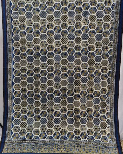 A close-up of a patterned textile or rug showing a repeating geometric hexagonal motif in blue, beige, and brown, with a decorative border at the bottom.