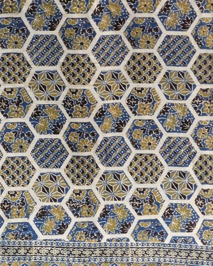 A close-up of a patterned textile or fabric with a repeating hexagonal motif in blue, gold, black, and off-white, plus a decorative border along the right edge.