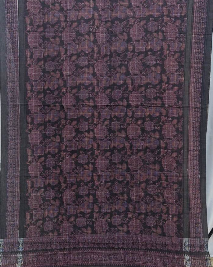 A dark purple and black patterned fabric, likely a saree or scarf, featuring a detailed floral and geometric motif with a striped border.