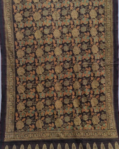 A dark brown or black silk saree with intricate gold, beige, and orange floral motifs and a detailed border.