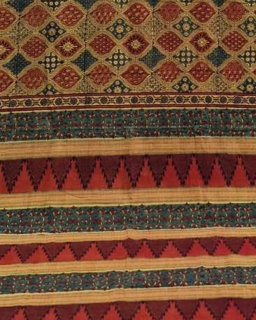 A close-up of a patterned textile or rug showing geometric bands with red, beige, and dark blue motifs.
