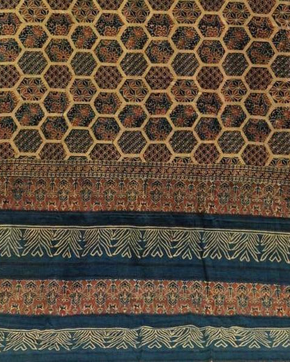A close-up of a patterned textile or fabric panel with a repeating honeycomb motif in dark brown, black, and tan, bordered by decorative bands in teal, rust orange, and cream.
