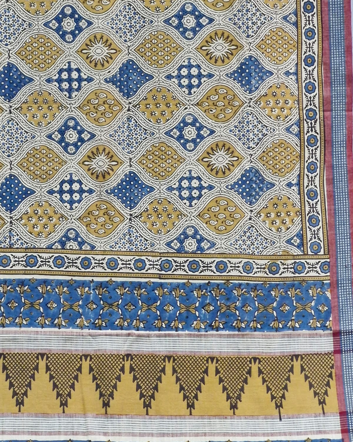 A close-up of a patterned textile or fabric panel with repeating geometric motifs in blue, mustard yellow, white, and black, plus decorative border bands.