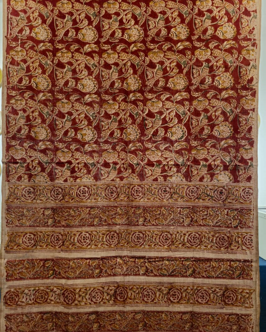 A large patterned textile or rug shown flat, featuring a deep red field with dense floral motifs in gold, beige, and muted green, plus a wide decorative border with repeating ornamental bands.