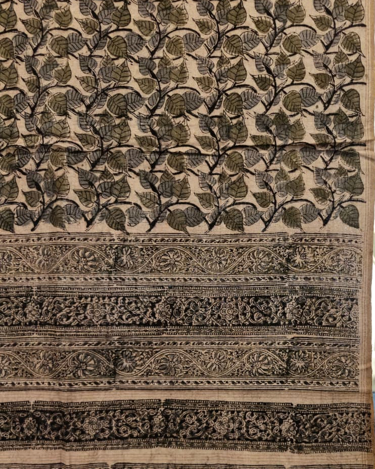 A close-up of a patterned textile or fabric panel with a beige base and dark charcoal/black leafy motifs, plus decorative horizontal bands with floral and geometric motifs.