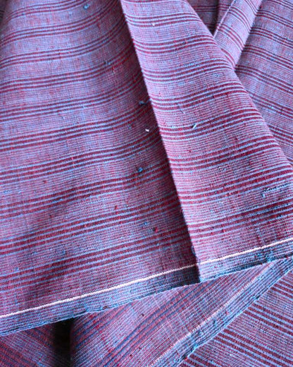 A close-up of draped fabric with a fine horizontal stripe pattern in muted burgundy red and dusty blue.