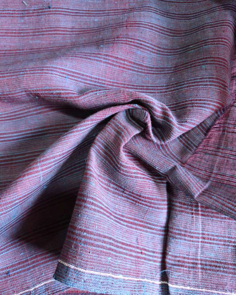 A close-up of draped striped fabric with horizontal bands in muted red, dusty blue, and gray, gathered in the center to show texture and weave.