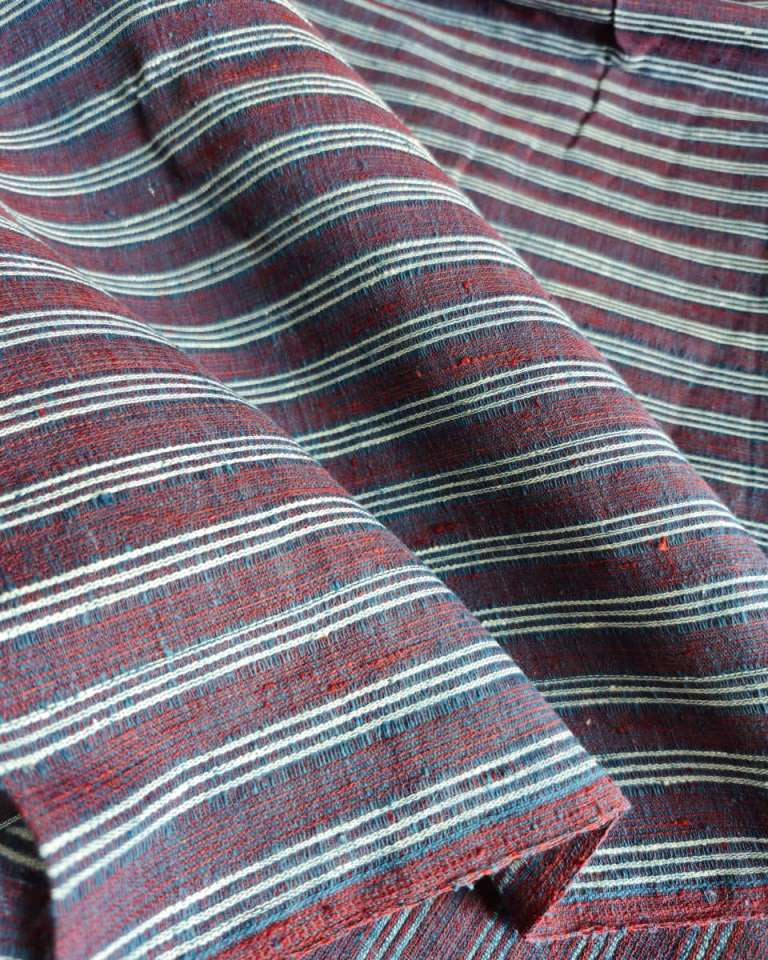 A close-up of draped striped fabric with horizontal red, navy, and off-white stripes, showing a textured woven material.