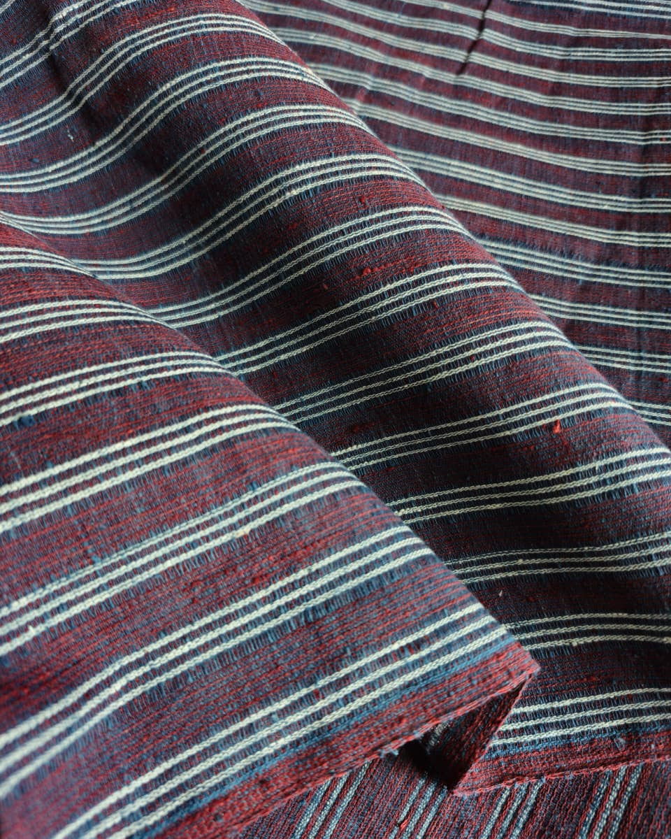 A close-up of striped fabric with horizontal bands in dark red, navy, and off-white, showing a textured woven material with soft folds.