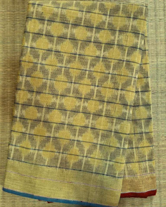 A folded yellow and brown patterned fabric, likely a saree or scarf, featuring a geometric ikat design with a blue and red border, laid flat on a woven straw mat.