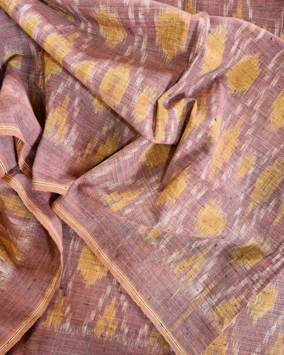 A close-up of a draped fabric with a dusty rose base and mustard yellow ikat-style motifs, showing the woven texture and border details.
