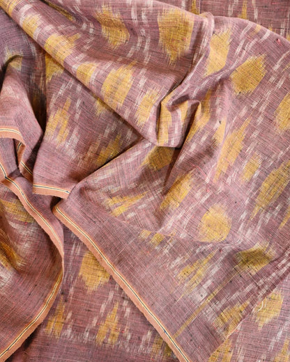 A close-up of a draped fabric with a dusty rose base and mustard yellow ikat-style motifs, showing the woven texture and border details.