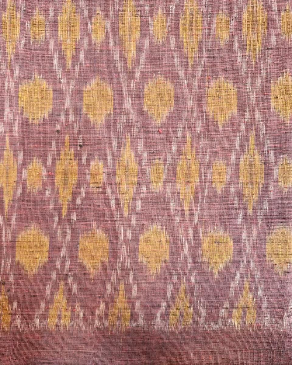 A close-up of a woven textile with a dusty mauve-pink base and repeating yellow ikat-style motifs, plus a narrow white dotted diagonal pattern running through the design.
