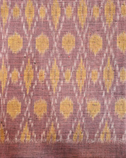 A close-up of a woven textile with a dusty mauve-pink base and repeating yellow ikat-style motifs, plus a narrow white dotted diagonal pattern running through the design.