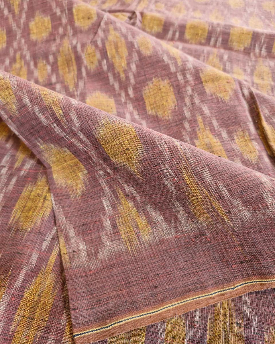 A close-up of draped fabric with a textured ikat pattern in dusty mauve, mustard yellow, and off-white.