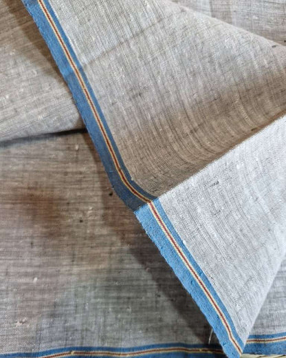 A close-up of a woven fabric with a light gray-beige body and blue borders accented by thin orange stripes, folded to show its texture and edge.
