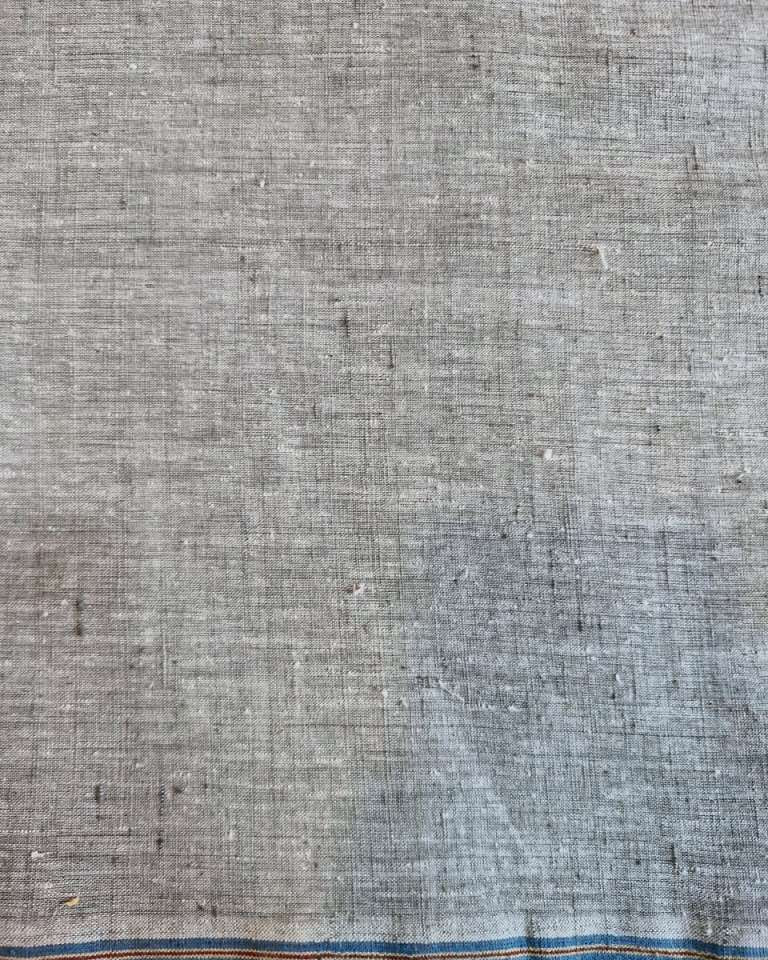A close-up of a textured gray fabric with a blue and orange stitched border along the bottom edge.