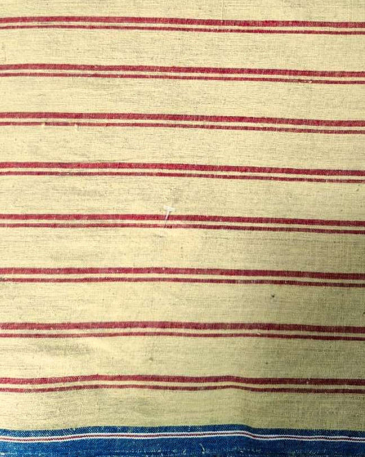 A close-up of a striped textile, likely a vintage striped blanket or towel, featuring horizontal red stripes on a cream-colored background, with a blue and white striped border at the bottom.