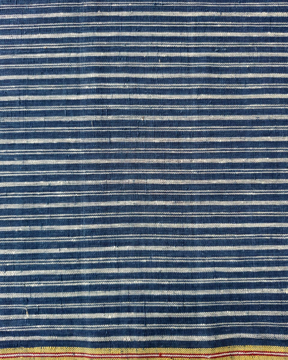 A close-up of a striped textile with alternating dark blue and off-white horizontal stripes, finished with a yellow-gold border and thin red accent lines near the bottom edge.