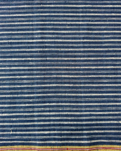 A close-up of a striped textile with alternating dark blue and off-white horizontal stripes, finished with a yellow-gold border and thin red accent lines near the bottom edge.