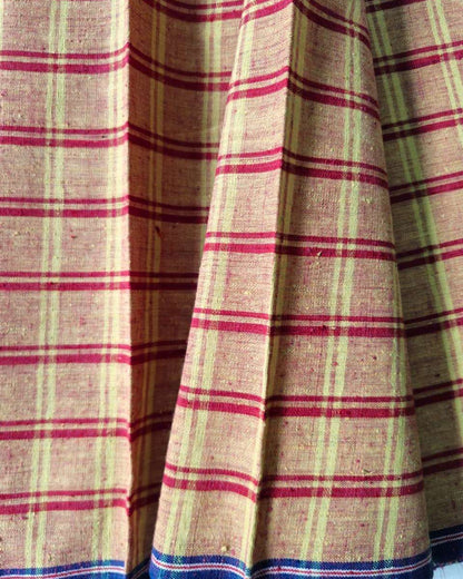 A close-up of a plaid fabric, likely a skirt or textile panel, featuring a beige base with red and light green stripes, finished with a blue and white striped border at the bottom.