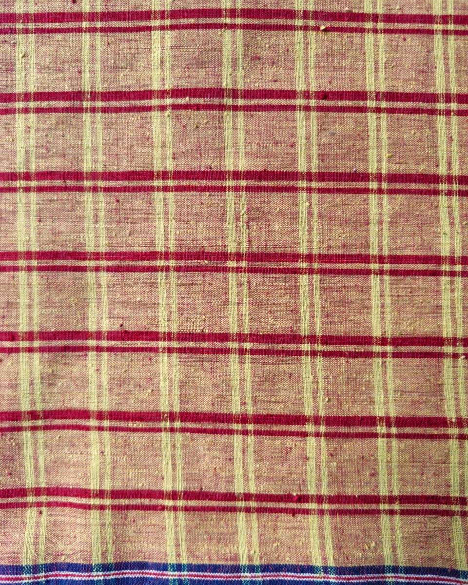 A close-up of a woven fabric with a plaid pattern, featuring a beige base with red horizontal stripes and vertical stripes in cream and dark blue.