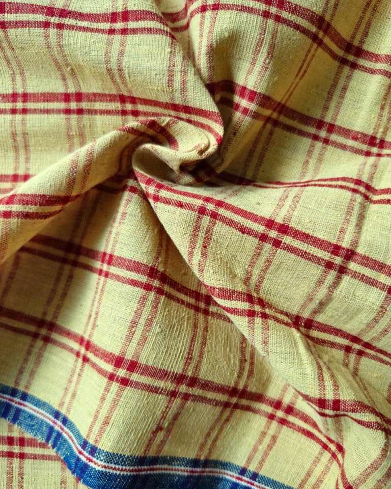 A close-up of a plaid fabric with a cream base, red intersecting stripes, and a blue striped border along the bottom edge.