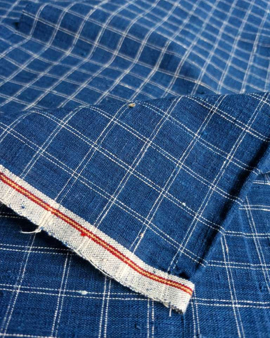 A close-up of blue fabric with a white windowpane plaid pattern and a folded hem showing a red and white striped inner edge.