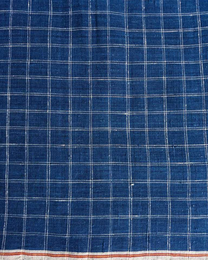 A close-up of a blue woven fabric with a white grid plaid pattern and a narrow orange-red stripe along the bottom edge.