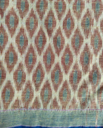 A close-up of a woven textile with an ikat-style diamond pattern in muted terracotta and pale blue on a warm beige ground, with a blue and green border along the bottom edge.