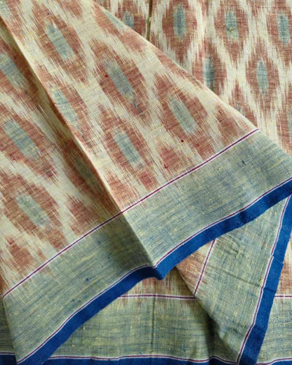 A close-up of a folded patterned fabric, likely a saree, featuring a rust-brown and beige ikat motif with a sage green border and blue and red stripes.