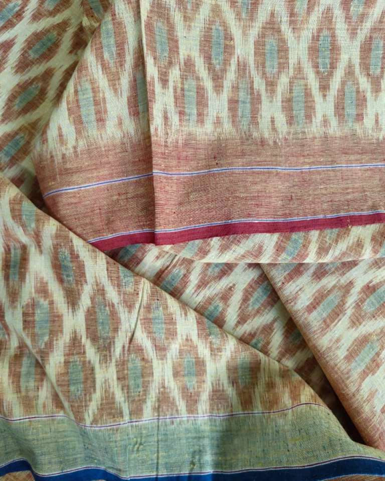 A close-up of a draped fabric with an ikat pattern in beige, brown, and muted teal, featuring a solid border with blue and red stripes.