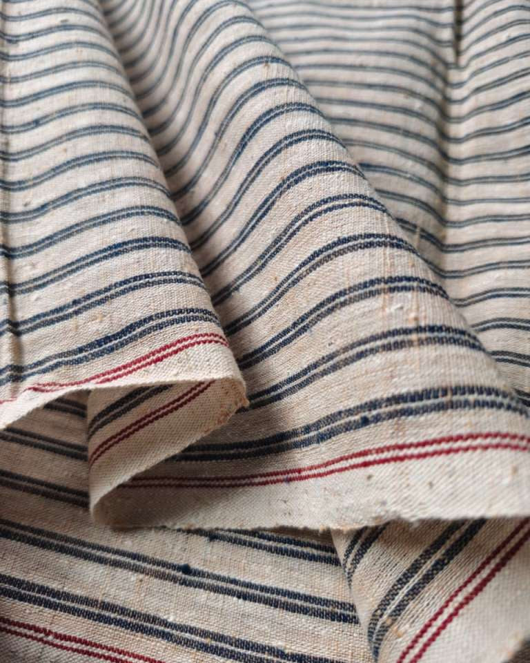 Close-up of draped fabric with a cream base and narrow horizontal stripes in dark blue and red.