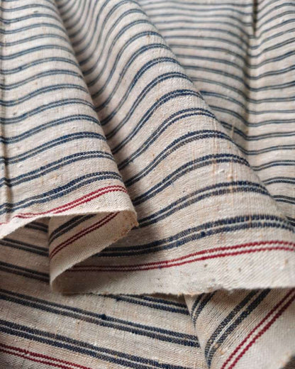 Close-up of draped fabric with a cream base and narrow horizontal stripes in dark blue and red.